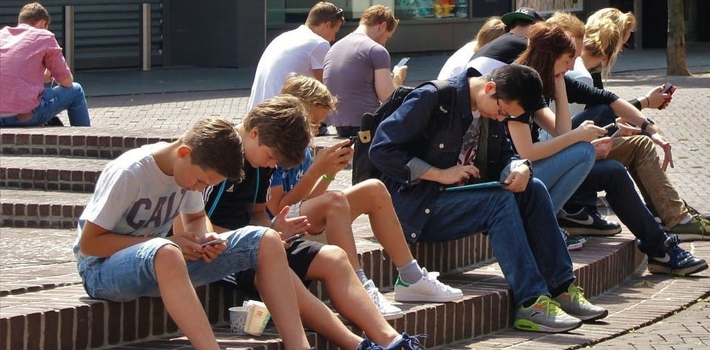 A group of kids and teens sitting at an outdooor plaza looking at their phones